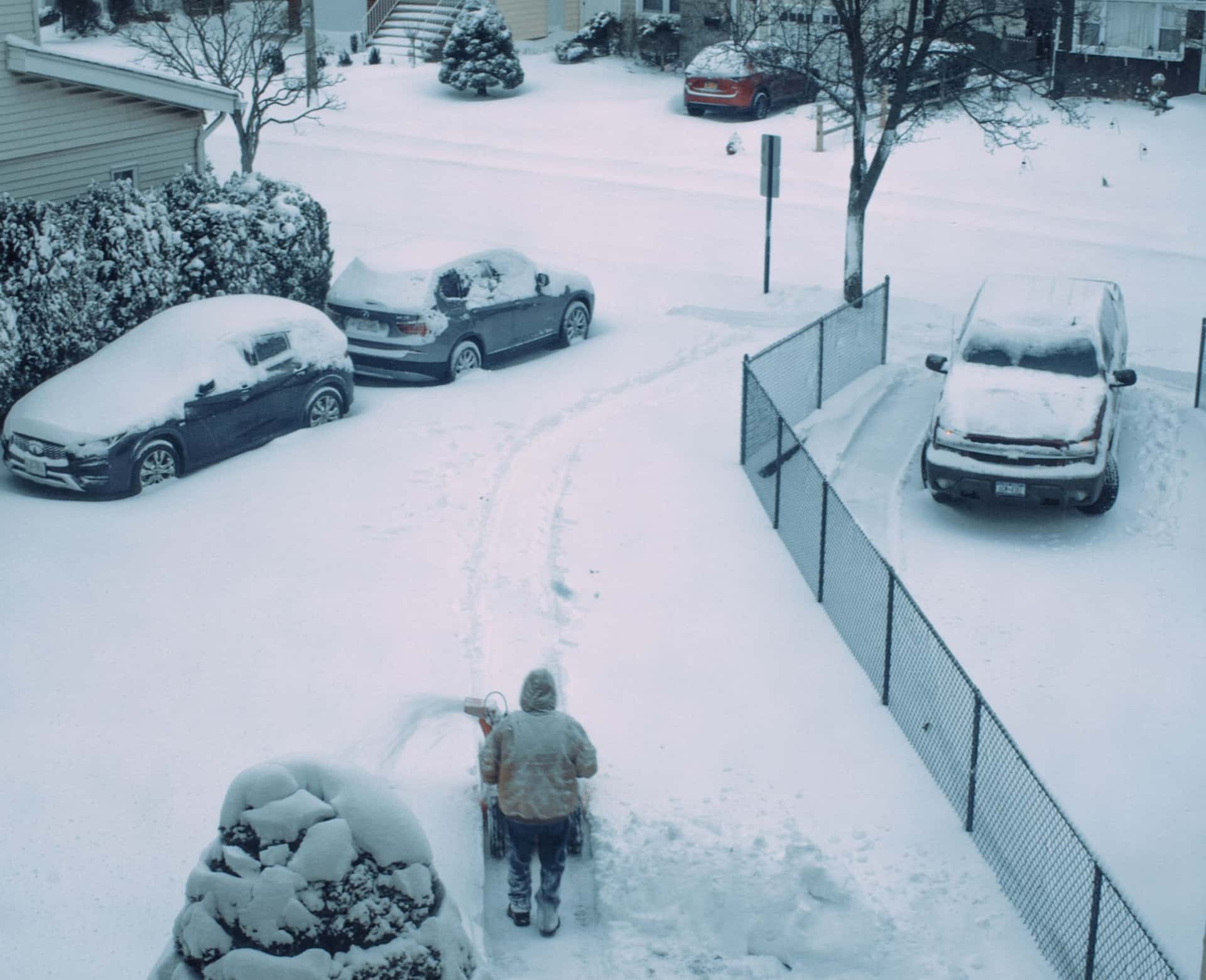 A person clearing snow from a car in a driveway