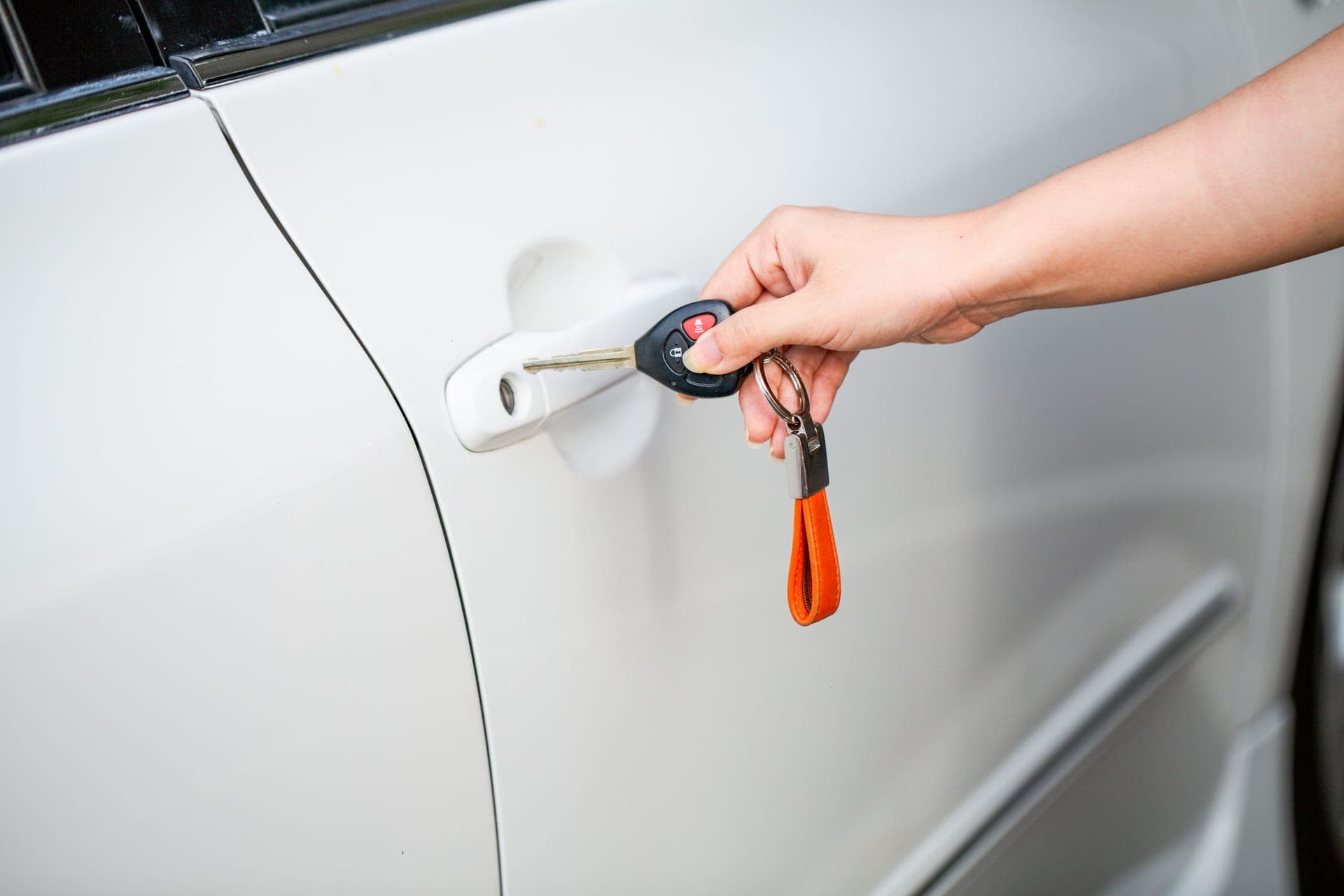 A person holding a car key beside a car door