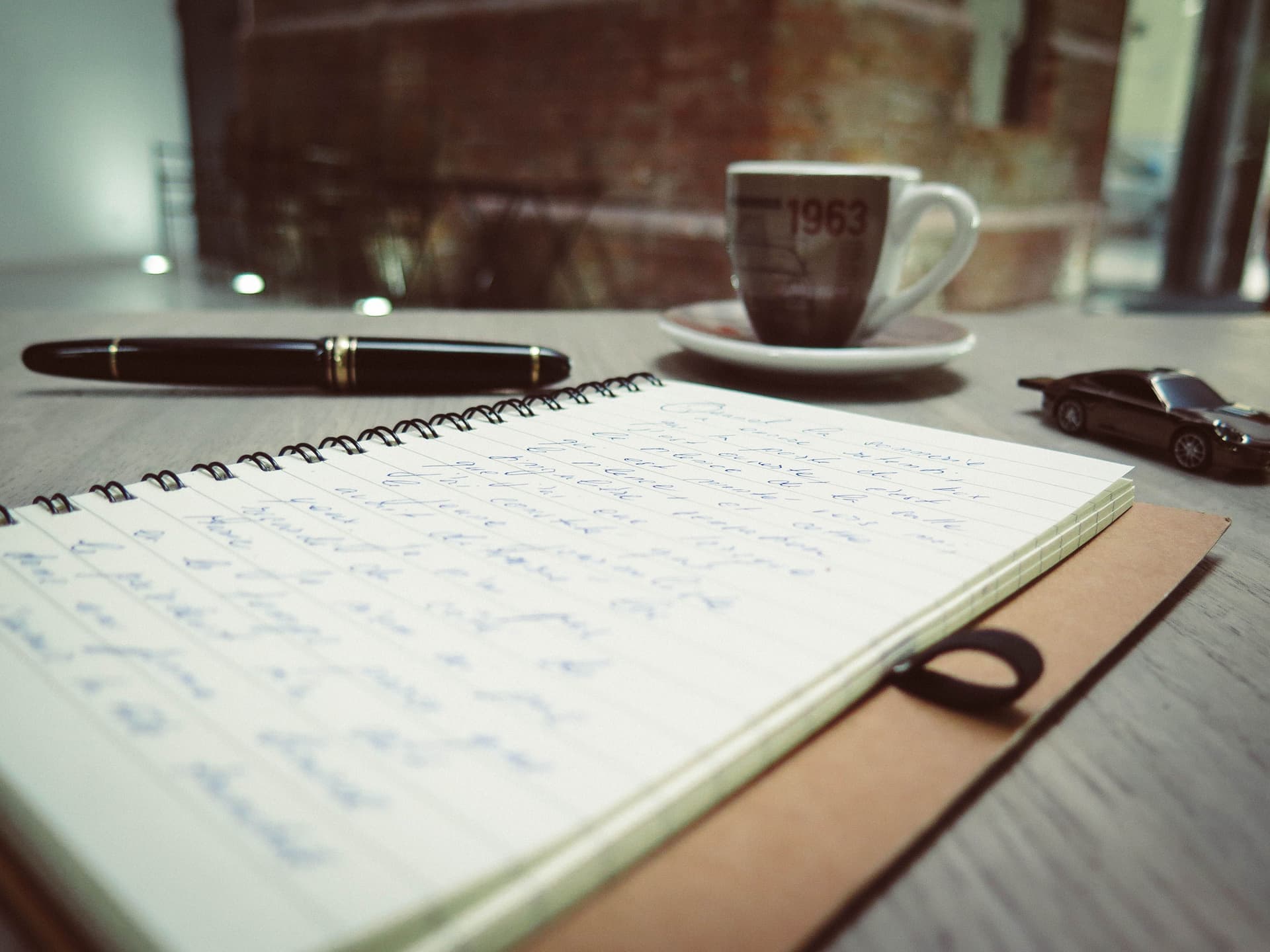 A notebook and pen beside a model car on a desk